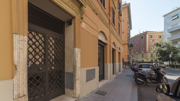 A building with a large, ornate metal gate and a number '69' sign. There are parked cars and a motorcycle on the sidewalk. - San Lorenzo Modern Flat (Rome)