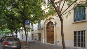 Un edificio con una puerta de madera grande, un letrero de estacionamiento y árboles a lo largo de la calle.