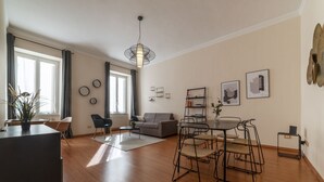Un amplio salón con sofá, mesa de comedor y sillas, una planta en maceta y obras de arte en las paredes.