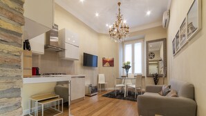 Una cocina moderna con televisor, un comedor con mesa y sillas, un sofá y una araña.