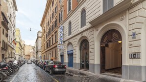 Una calle adoquinada bordeada de automóviles estacionados y edificios históricos, incluyendo un letrero de 'Sport Italia'.