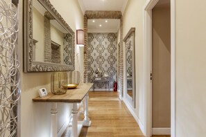 A hallway with a wooden table, a large mirror, patterned wallpaper, and a fire extinguisher.