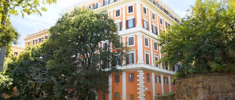 Un edificio de varios pisos con fachada de piedra, autos estacionados y árboles en la parte delantera.