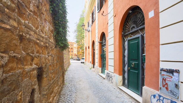 A narrow cobblestone street flanked by buildings with arched windows and a green door.