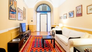 A hotel lobby with a TV, white sofa, patterned rug, and framed pictures on the walls.