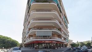 A multi-story hotel with balconies, a red awning, and parked cars.