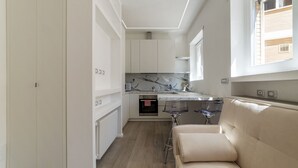 A compact kitchen with white cabinets, a marble backsplash, and a built-in oven.