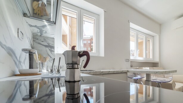A modern kitchen with a marble countertop, a kettle, and a dining area with a glass table and chairs.