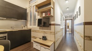 A modern kitchen with dark cabinets, a built-in oven, and a wooden countertop. There is a TV mounted on the wall and a small wooden shelf with kitchen items. - Roma Termini Big Apartment (Rome)