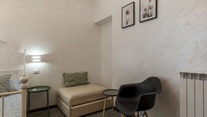 A small, neatly arranged room with a bed, a sofa, a chair, a small table, and two framed pictures on the wall. - Roma Termini Big Apartment (Rome)