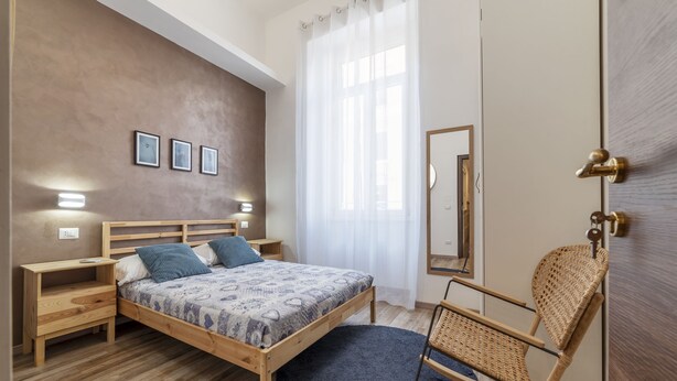 A bedroom with a wooden bed, bedside tables, a mirror, and a rocking chair. - Roma Termini Big Apartment (Rome)