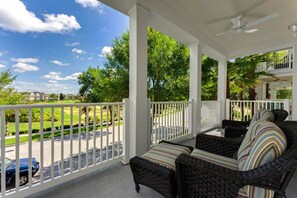 A covered porch with wicker furniture and a view of a green lawn and houses in the background.