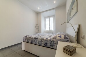 A bedroom with a bed, a desk, a lamp, a radiator, and a window. - Porta Pia & Villa Torlonia Apartment with Balcony (Rome)