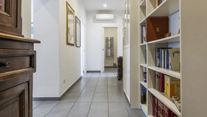A hallway with a wooden cabinet, a bookshelf with books, and a tiled floor.