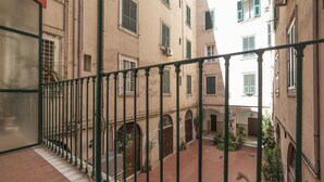 A courtyard with a green metal railing, potted plants, and buildings with arched doorways and windows.
