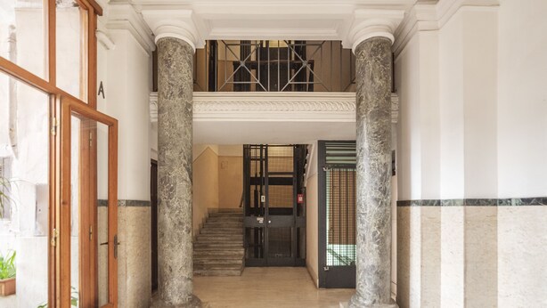 A grand entrance with marble columns, a staircase, and a security gate.