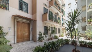 A courtyard with potted plants, a wooden door, and a tiled floor. - San Giovanni Apartment with Balcony (Rome)