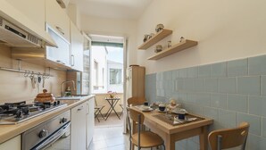 A compact kitchen with a stove, oven, and dining table with chairs. There is a window providing natural light and a view of the outside. - San Giovanni Apartment with Balcony (Rome)