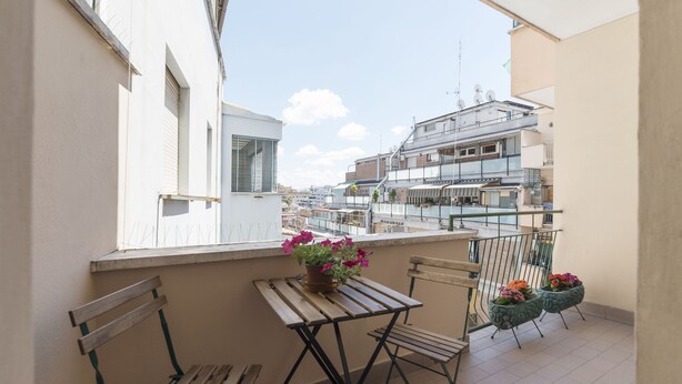A balcony with a wooden table and chairs, potted plants, and a view of surrounding buildings. - San Giovanni Apartment with Balcony (Rome)