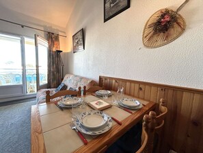 A dining area with a wooden table set for four, a sofa, and a large window with curtains.