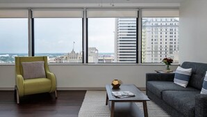 A modern living room with a city view, a green armchair, a gray sofa, and a coffee table. - 16th FL Bold CozySuites w/pool, gym, roof #1 (Dallas)