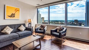 Una sala de estar moderna con un sofá gris, dos sillones, una mesa de centro y un ventanal con vistas a la ciudad.