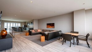 Una sala de estar moderna con un sofá modular, una mesa de comedor con sillas y una cocina al fondo.