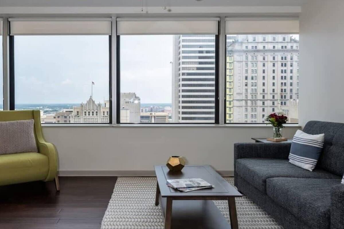 A modern living room with a city view, a green armchair, a grey sofa, and a coffee table.