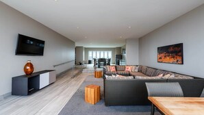 A modern living room with a sectional sofa, a flat-screen TV, and a dining area with a table and chairs. - 16th FL Bold CozySuites w/pool, gym, roof #3 (Dallas)