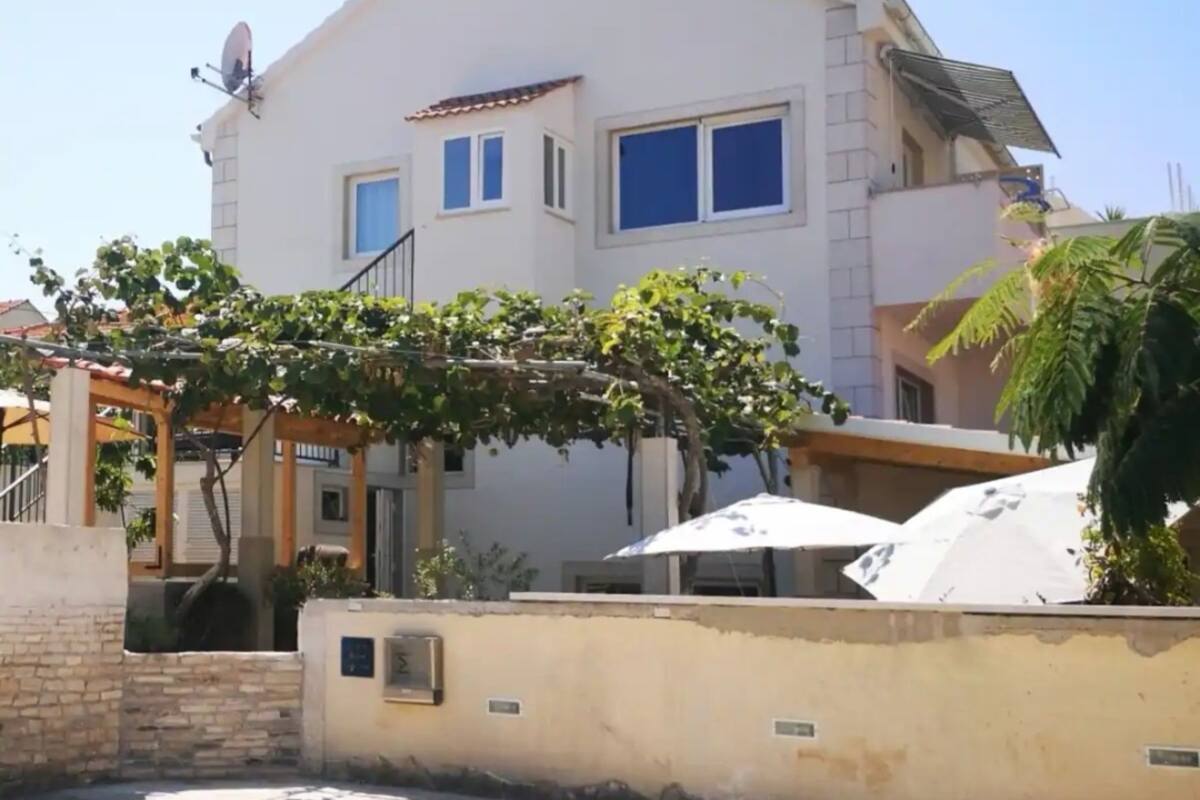 A two-story building with a white facade, blue windows, and a pergola with green vines.