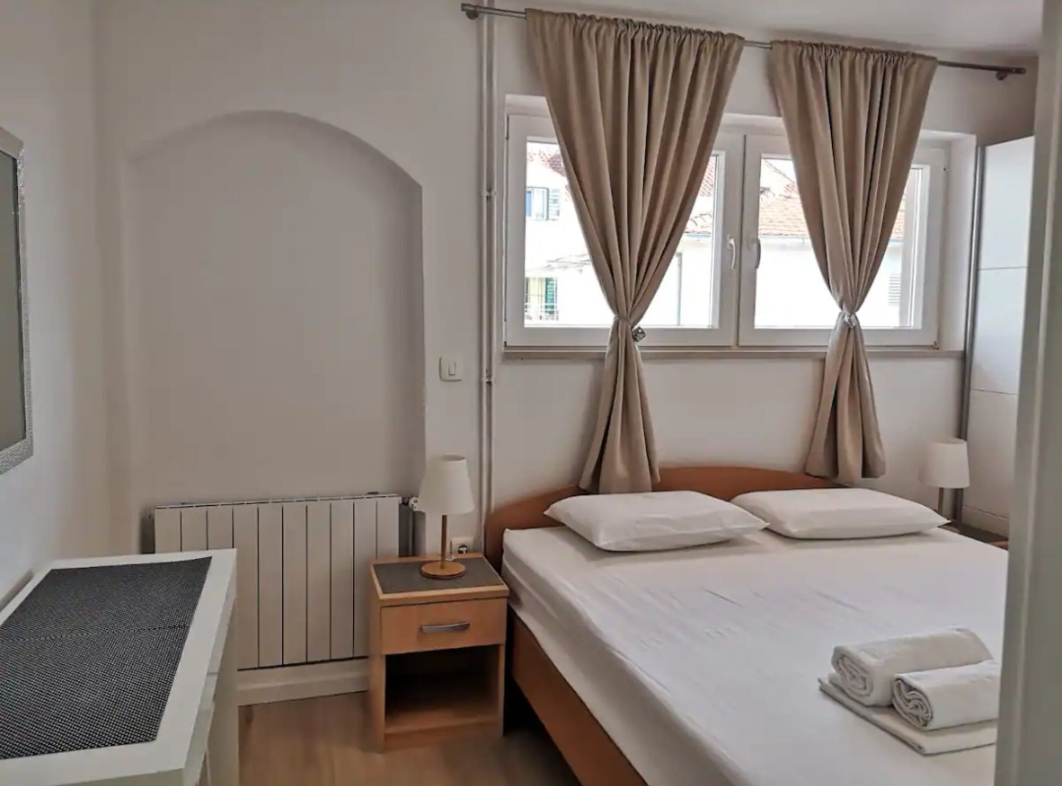 Een hotelkamer met een bed, nachtkastje, lamp, radiator en gordijnen.