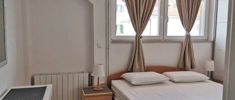 Een hotelkamer met een bed, nachtkastje, lamp, radiator en gordijnen.