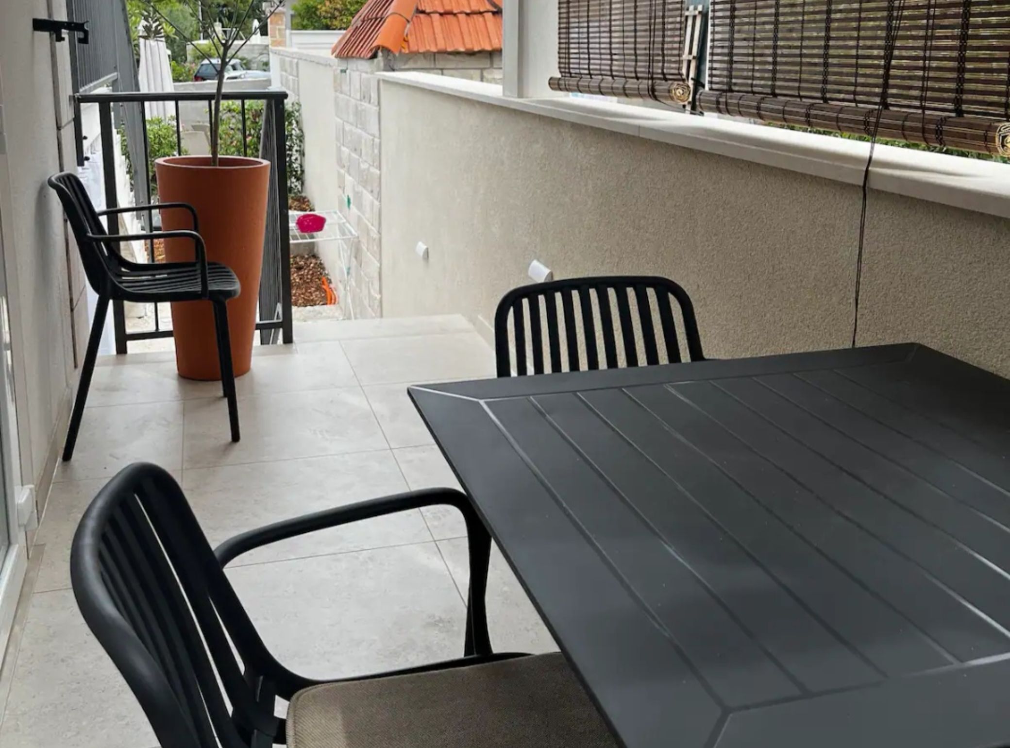 A balcony with a table and chairs, a potted plant, and a window with blinds.