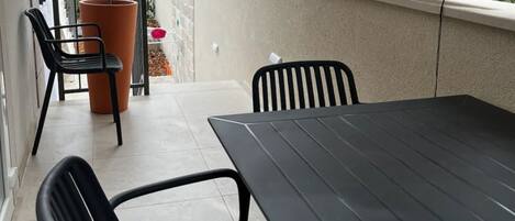 A balcony with a table and chairs, a potted plant, and a window with blinds.