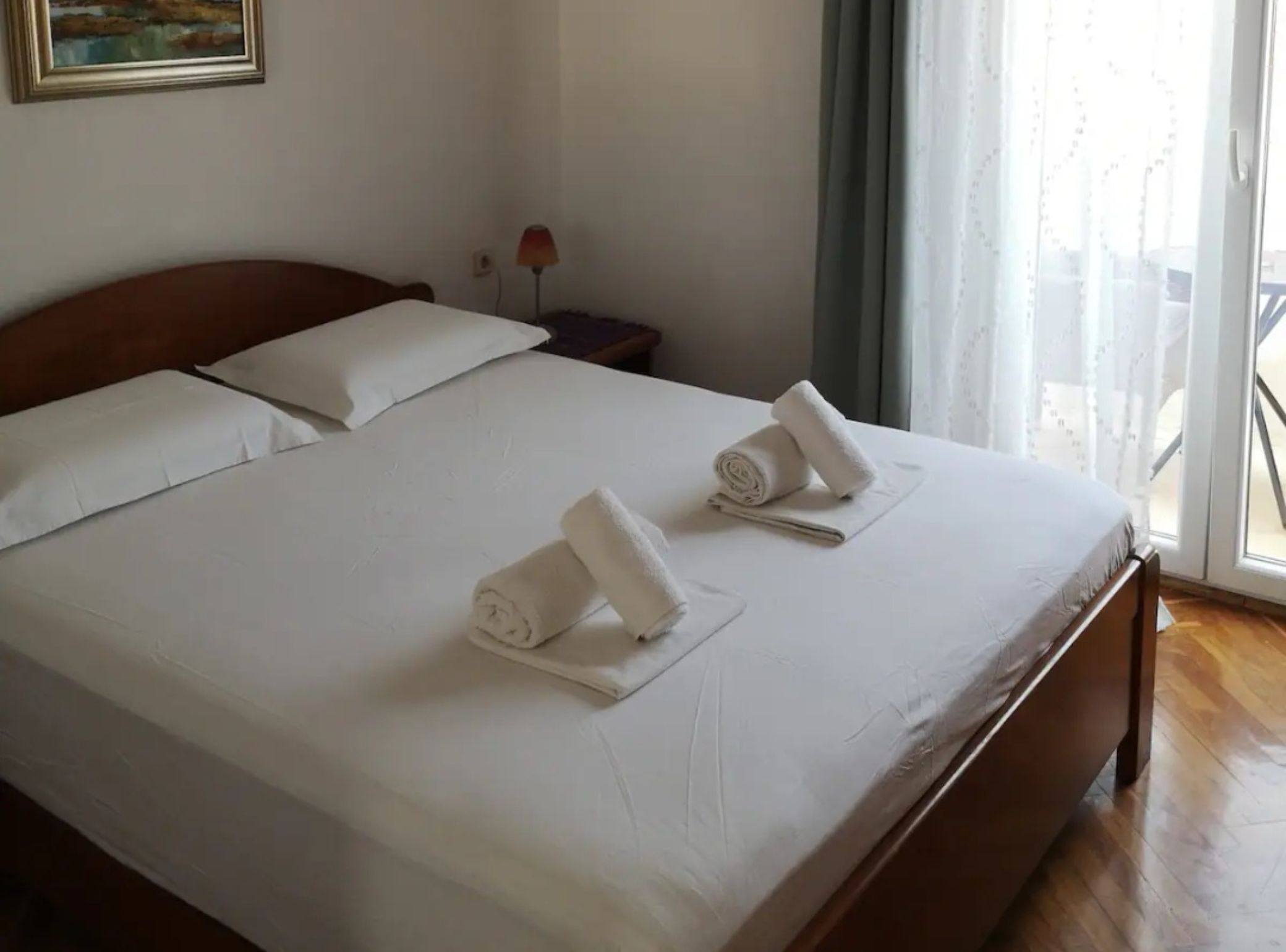 Una cama bien hecha con sábanas blancas y dos toallas enrolladas sobre la cama.