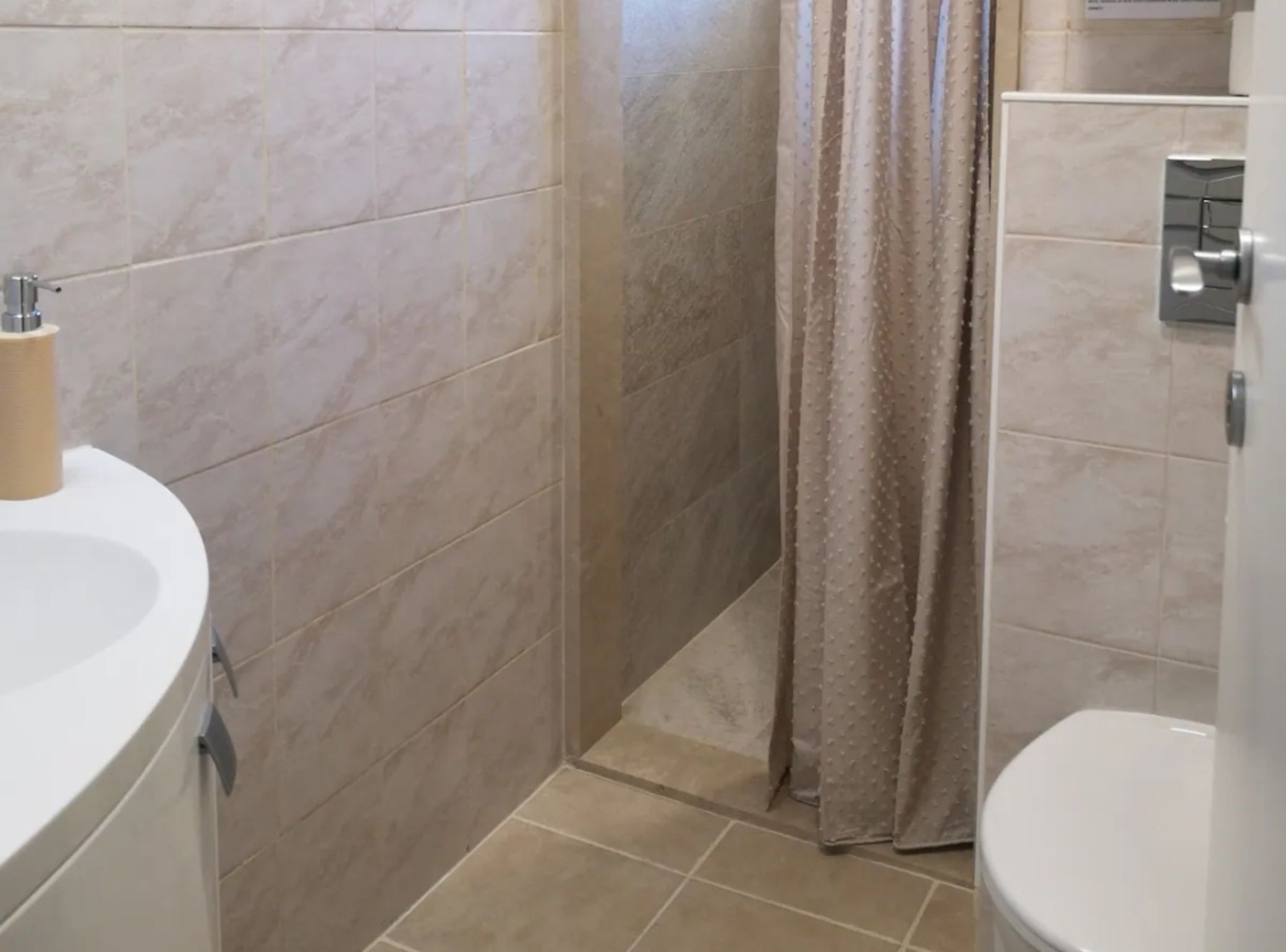 Ett badrum med ett vitt handfat, beige kakel och en duschdraperi.