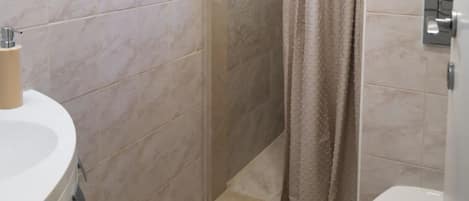 A bathroom with a white sink, beige tiles, and a shower curtain.