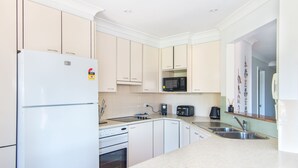 A modern kitchen with white cabinets, a refrigerator, a microwave, a coffee maker, and a toaster. - Horizons 8 on the lake (forster)