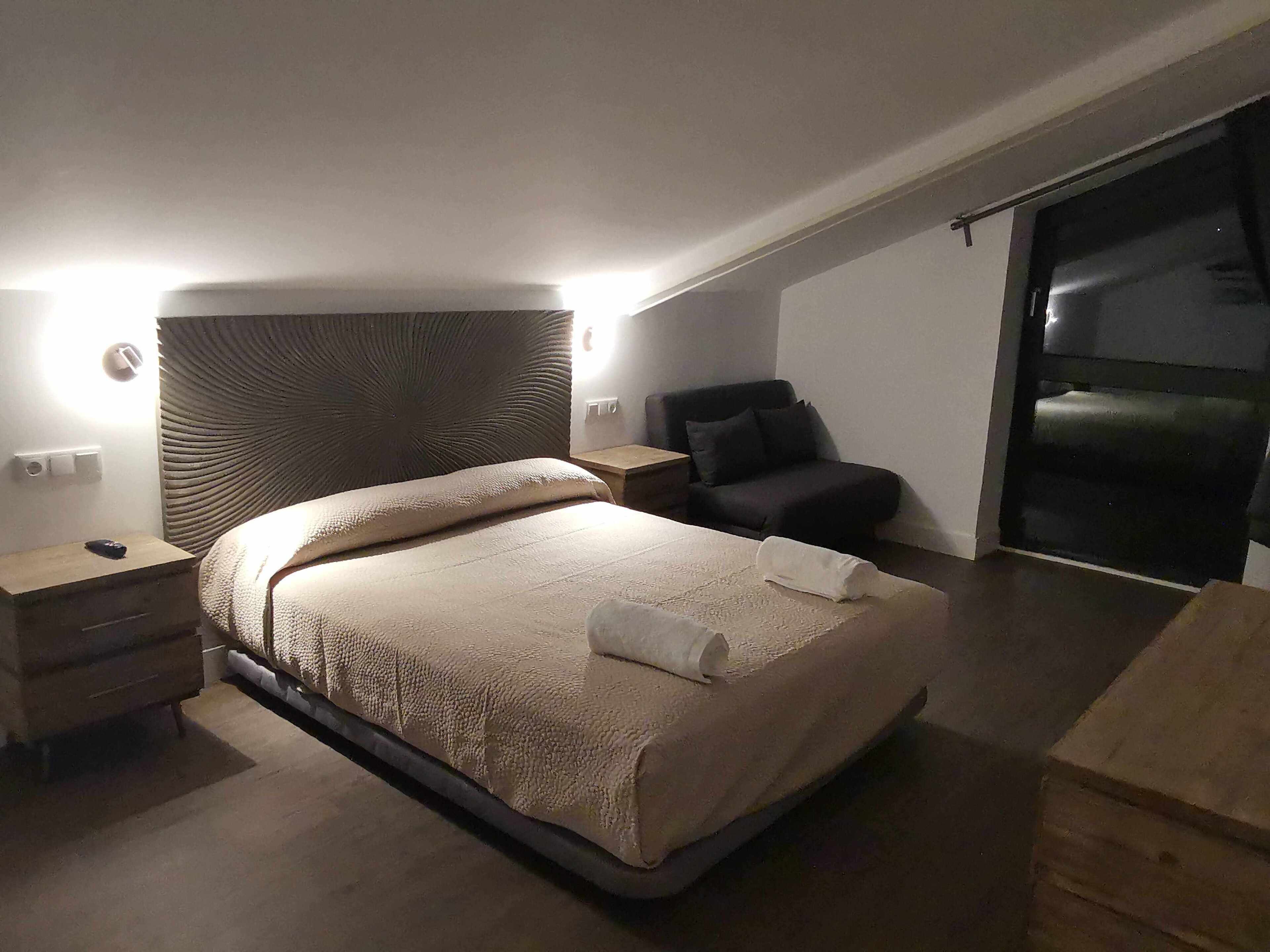 A bedroom with a bed, bedside tables, a chair, and a large window.