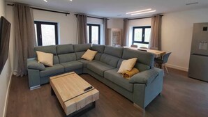 A modern living room with a sectional sofa, a wooden coffee table, and a dining area with a table and chairs. - 3 BEDROOM APARTMENT VILLA MAREL (Cerdillo)