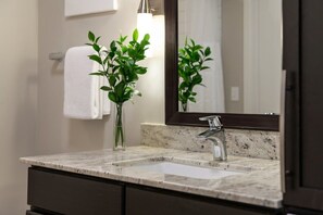 A bathroom with a marble sink, a modern faucet, and a mirror. There is a plant in a clear vase on the counter.
