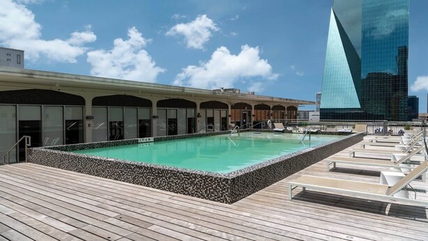 A rooftop pool with a tiled edge, wooden deck, and lounge chairs. - Downtown Dallas CozySuites w/ roof pool, gym #6 (Dallas)