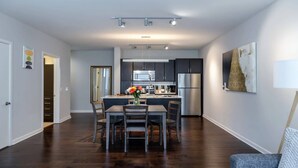 A modern kitchen with dark cabinets, stainless steel appliances, and a dining area with a table and chairs. - Downtown Dallas CozySuites w/ roof pool, gym #6 (Dallas)
