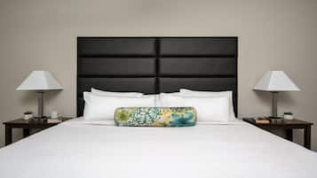 A neatly made bed with white linens, a black padded headboard, and a colorful pillow. There are two bedside tables with lamps and small plants.