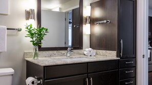 Un baño moderno con lavamanos de mármol, muebles oscuros y un espejo grande.