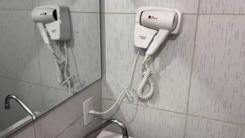 Un baño con un lavamanos blanco, un espejo y dos secadores de pelo fijados en la pared.