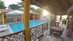 A poolside area with a wooden table and chairs, a pool, and a covered seating area with umbrellas. - Pousada Uba-Rio Porto de Galinhas (Ipojuca)