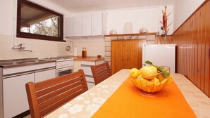 Eine kleine Küche mit weißen Schränken, einem Holztisch mit orangefarbener Tischdecke und einer Obstschale auf dem Tisch.