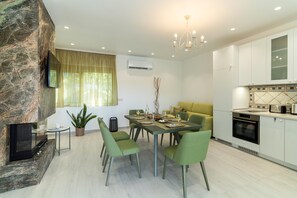 Uma cozinha moderna com forno embutido, área de jantar com cadeiras verdes e parede de pedra decorativa.