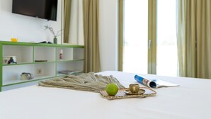 Een hotelkamer met een bed, een flatscreen televisie aan de wand, een groen kastje met diverse spullen en een raam met gordijnen.